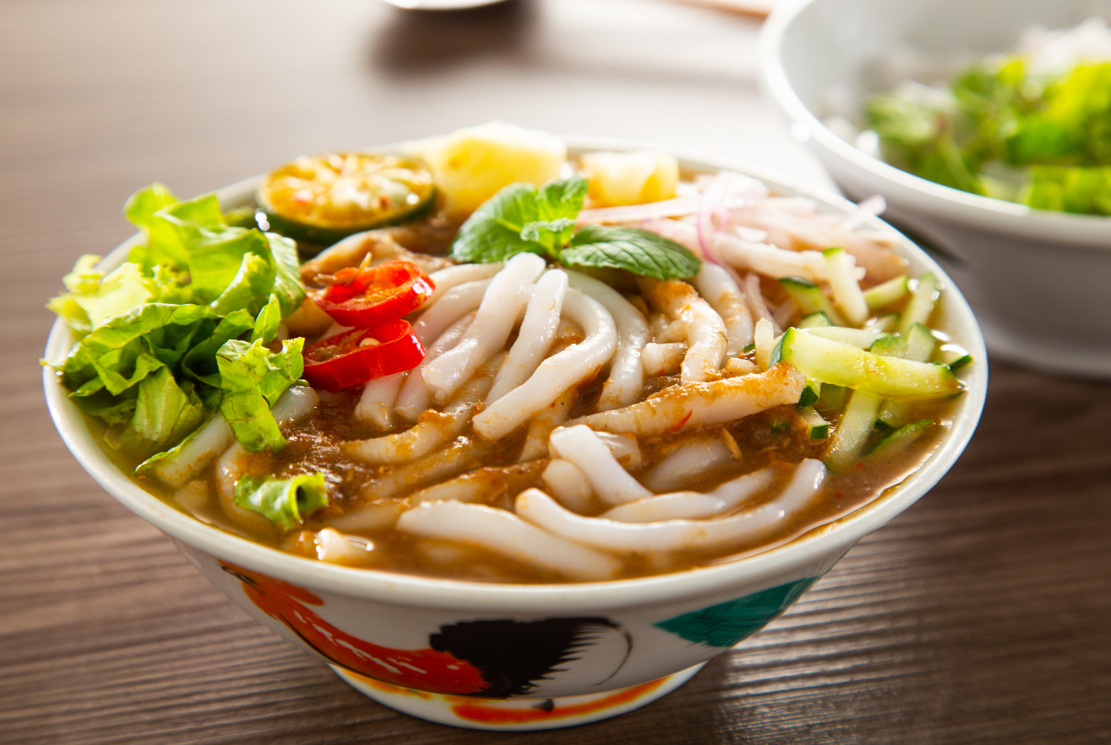 A bowl of laksa with thick rice noodles and fresh garnishes